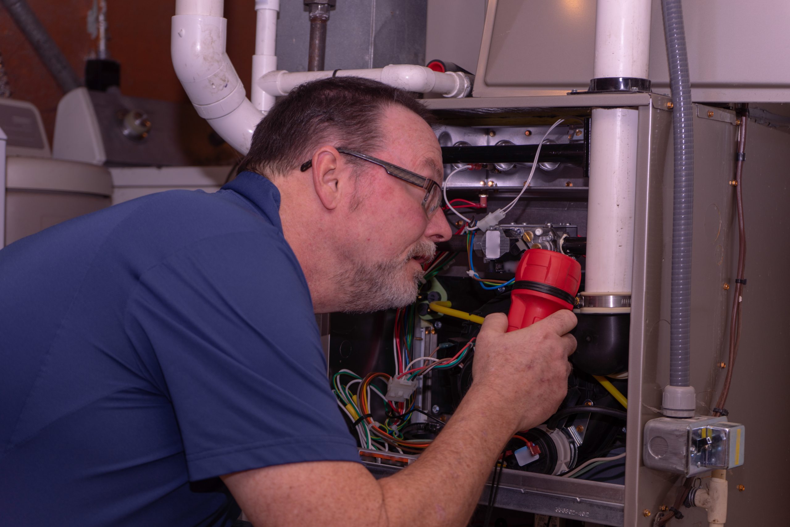 Hvac,Tech,Looking,Over,A,Gas,Furnace,Blue,Shirt HVAC technician inspecting furnace